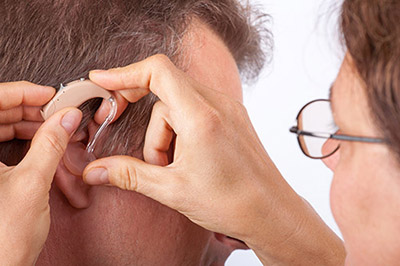 Doctor fitting a senior man patient with hearing aid